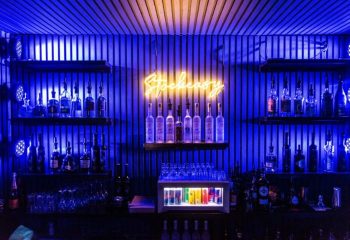 Montreal gay bar stock. Blue-lit bar shelves stocked with liquor bottles. Stockeasy neon sign. Gay stripper liveshow venue. Travel advice.