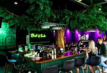 Bar Stock Montreal: A vibrant gay bar with lush greenery, neon lights, and a lively atmosphere. Perfect for a night out in Montreal.