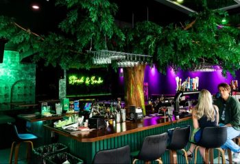 Bar Stock Montreal: A vibrant gay bar with lush greenery, neon lights, and a lively atmosphere. Perfect for a night out in Montreal.