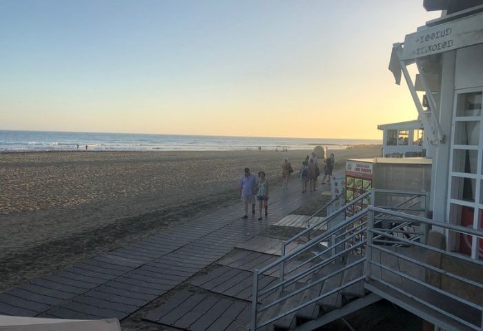Gran Canaria gay beach scene at sunset. People stroll along the boardwalk by a bar near the beach, enjoying the evening light.