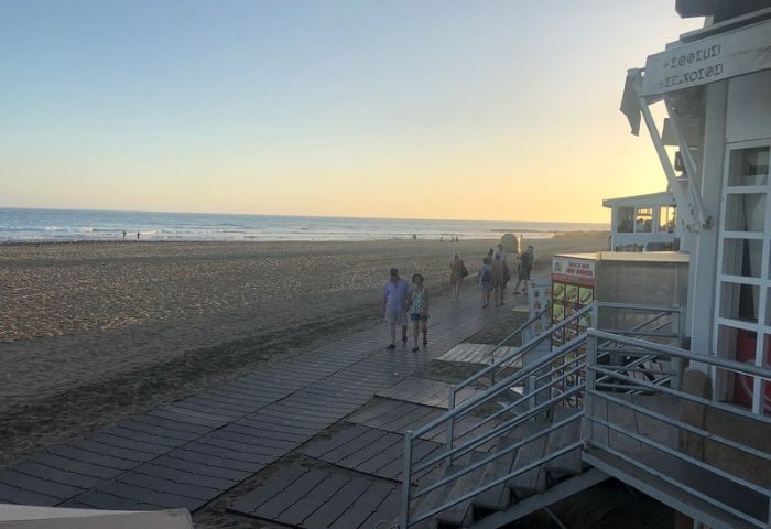Gran Canaria gay beach scene at sunset. People stroll along the boardwalk by a bar near the beach, enjoying the evening light.