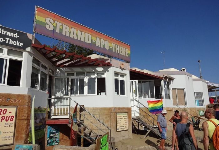 Strand-Apo-Theke gay bar in Gran Canaria. Beachside bar with rainbow flag. Gay travel destination for men. LGBTQ+ friendly beach bar.