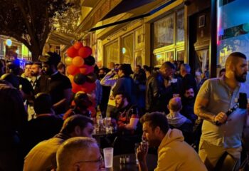 Gay bar TR3S in Lisbon, Portugal. Outdoor patio area filled with gay men drinking and socializing at night. Balloons decorate the entrance.