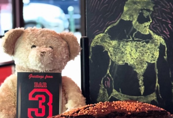 Bar TR3S Lisboa still life: Teddy bear holding a Greetings from Bar 3 card, next to a drawing of a muscular man on a chalkboard.