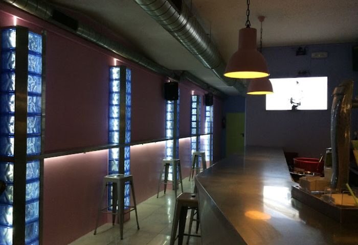Interior of Barbanarama Gay Bar in Madrid. Features include a bar counter, stools, and decorative glass block columns with blue lighting.