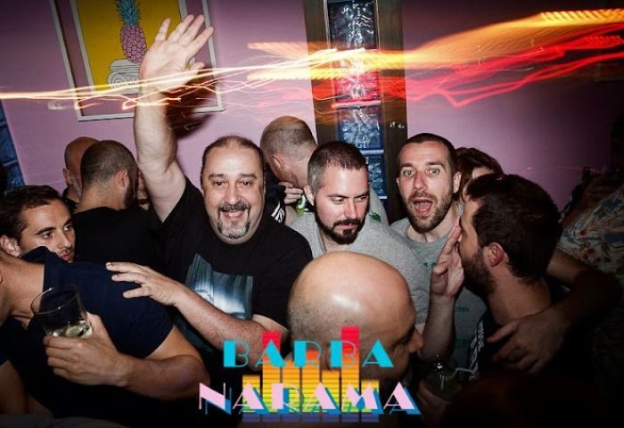 Crowded scene at Barbanarama, a gay bar in Madrid. Men are smiling, waving, and enjoying the vibrant atmosphere. Gay travel.