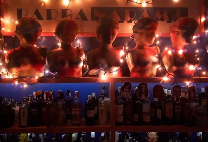 Barbanarama Gay Bar in Madrid: Busts on a shelf, adorned with string lights, above liquor bottles. Gay travel destination.