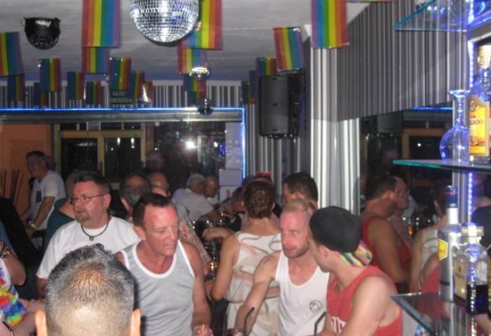 Inside Barcode, Benidorm's gay bar. Rainbow flags, disco ball, and a crowd of men create a lively atmosphere for gay travel in Benidorm.