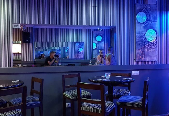Barcode Gay Bar in Benidorm. Interior view of the bar with tables, chairs, and people at the counter. Blue lighting. Gay travel advice.