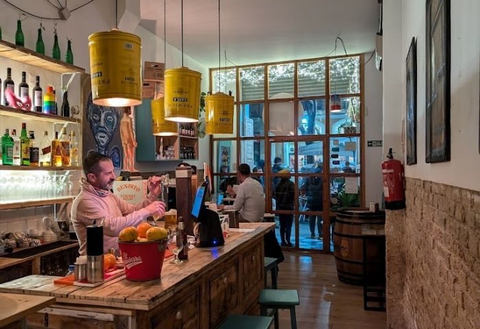 Inside Bardaixa Gay Bar in Barcelona: Bartender pouring a drink at the wooden bar, unique lighting, and a lively atmosphere.