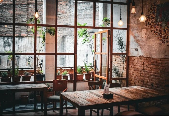 Interior of Bardaixa Gay Bar in Barcelona. Rustic wooden tables and chairs, exposed brick, and plants create a cozy atmosphere.