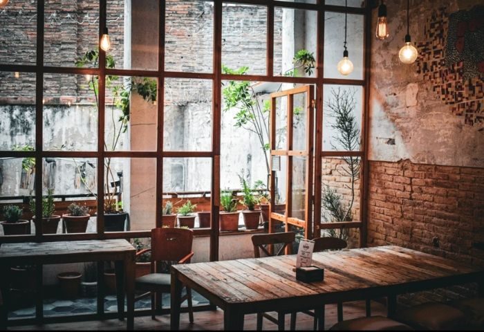 Interior of Bardaixa Gay Bar in Barcelona. Rustic wooden tables and chairs, exposed brick, and plants create a cozy atmosphere.