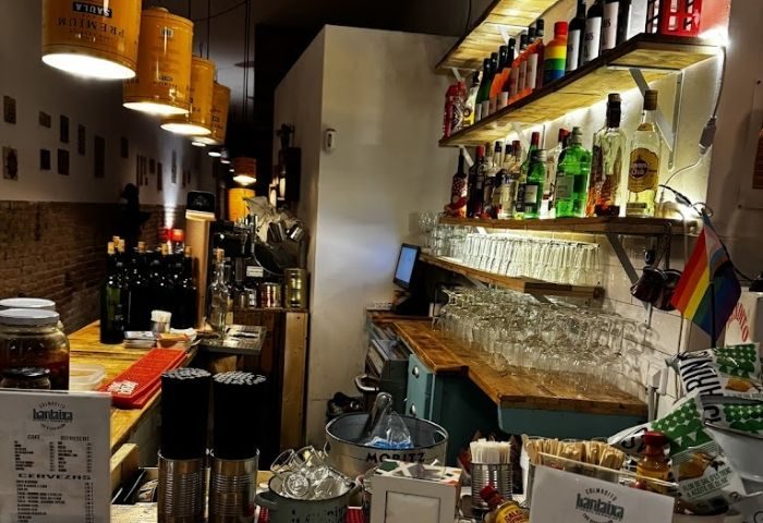 Interior of Bardaixa Gay Bar in Barcelona. Shelves of liquor, glasses, and a rainbow flag. Gay travel advice for Barcelona.