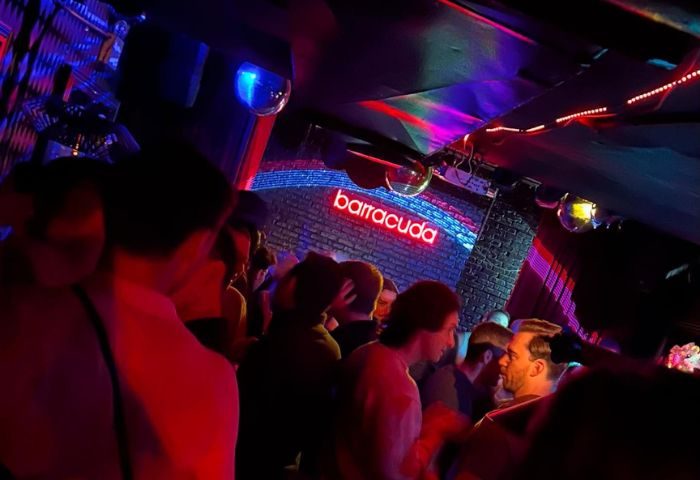 Inside Barracuda Lounge, a New York gay bar. People mingle under disco balls and neon lights. Nightlife scene for gay men's travel.