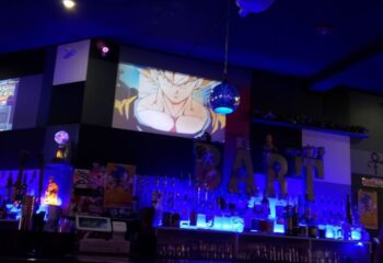Bart Lounge Bar interior. Anime on screen. Gay bar with blue lighting, bottles, and decor. Travel advice for gay men.