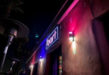 Night view of Bart Lounge location. Neon sign glows above the entrance. Heaters provide warmth on the patio of this gay bar.