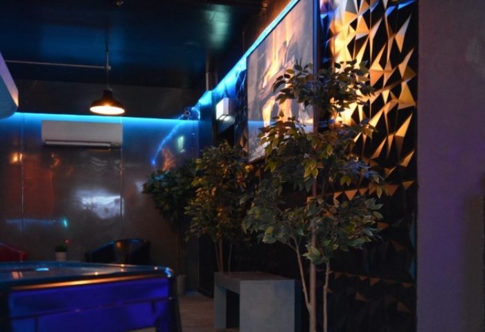 Basement Complex Manchester interior. Stylish gay travel spot with blue lighting, plants, and geometric wall decor. Modern design.