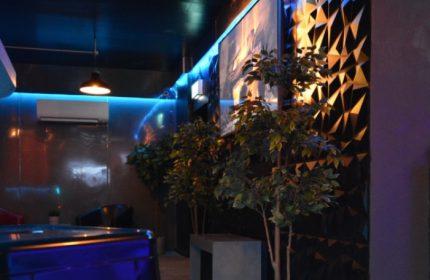 Basement Complex Manchester interior. Stylish gay travel spot with blue lighting, plants, and geometric wall decor. Modern design.