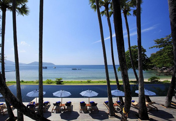 Beachfront pool villas at The Naka Phuket Villa, perfect for gay honeymoon couples. Ocean view with palm trees, umbrellas, & lounge chairs.