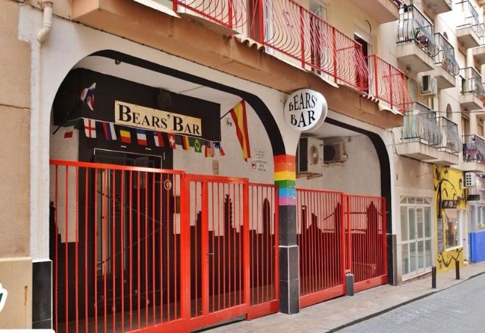 Bear's Bar in Benidorm, a gay-friendly destination. Red gates, rainbow pillar, and international flags adorn the entrance for drinks & party.