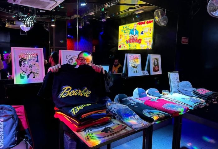 Bearbie Gay Club in Madrid: Man holding Bearbie shirt at a merchandise stand with hats and art prints in a dark, club-like setting.