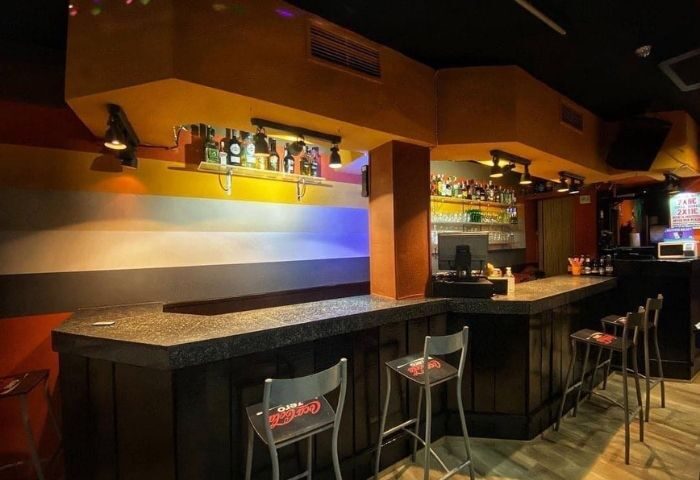 Interior of Bears Bar, a gay bar in Madrid. Bar stools line the counter, bottles on shelves. Nightlife for gay men travelers.