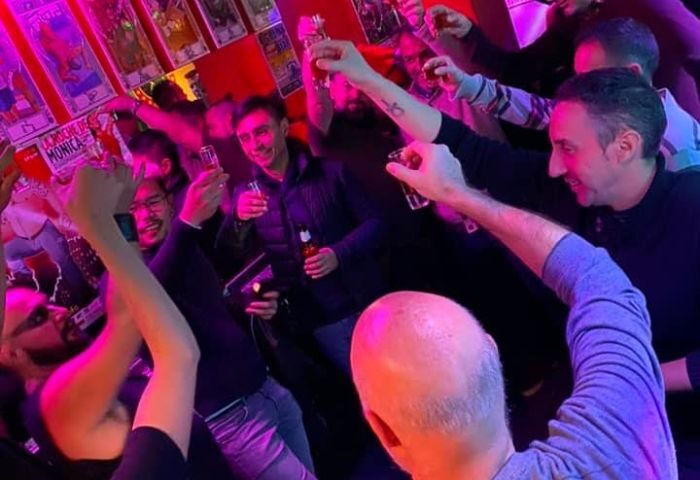 Gay men toasting at Bears Bar, a popular gay bar in Madrid. The bar is crowded, with people holding up shot glasses and smiling.