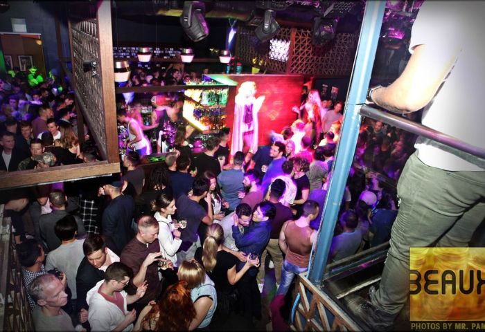 Beaux Gay Bar in San Francisco: A crowded, multi-level gay bar with a drag queen performing on stage. People are dancing and socializing.