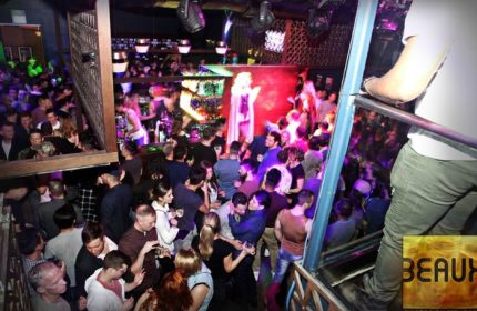 Beaux Gay Bar in San Francisco: A crowded, multi-level gay bar with a drag queen performing on stage. People are dancing and socializing.