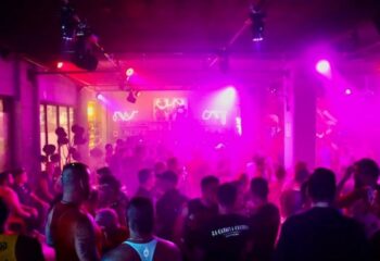 Beefcakes Gay Bar in Puerto Vallarta: A crowded dance floor with pink lighting, silhouettes of men, and neon bar signs.