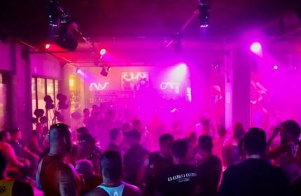 Beefcakes Gay Bar in Puerto Vallarta: A crowded dance floor with pink lighting, silhouettes of men, and neon bar signs.