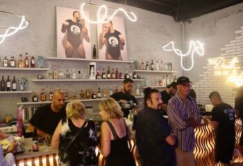 Inside Beefcakes Gay Bar in Puerto Vallarta, Mexico. Bartenders and patrons at the bar. Neon lights and beefcake art. Gay travel.