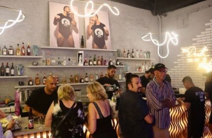 Inside Beefcakes Gay Bar in Puerto Vallarta, Mexico. Bartenders and patrons at the bar. Neon lights and beefcake art. Gay travel.