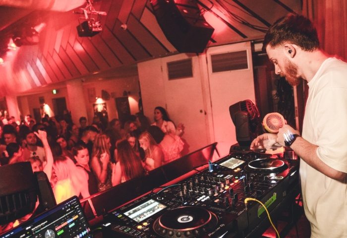 DJ at Beresford Hotel Sydney, a popular gay-friendly venue. Red lighting, crowded dance floor. Gay men travel advice.