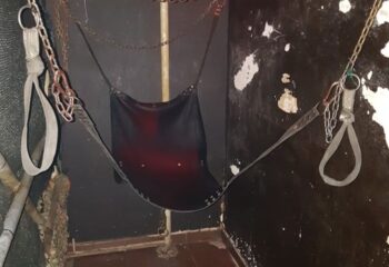 Berlin Dark Gay Cruise Club in Barcelona: A black leather sling hangs with chains in a dark room, part of a gay cruising area.