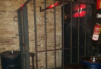Interior of Berlin Dark gay cruise club in Barcelona. Cage with rings, brick wall, and dark ambiance. Gay travel destination.