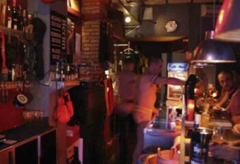 Inside Berlin Dark gay cruise club in Barcelona. Bare-chested men at the bar, intimate atmosphere. Gay travel.