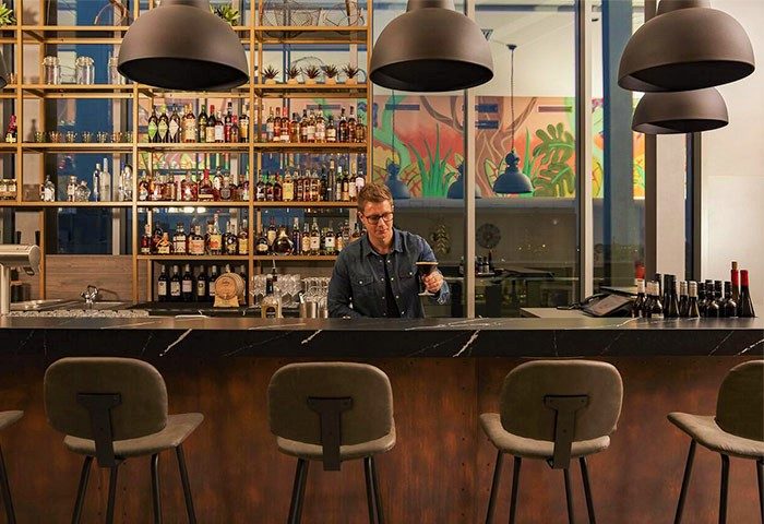Hotel Indigo Berlin East Side Gallery bar with bartender holding drink. Great reviews, popular cheap hotel for gay men travel advice.