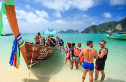 Koh Phi Phi's Cobble Beach Hotel: Beachfront scene with gay travelers disembarking a longtail boat on a sunny day. Tropical paradise.