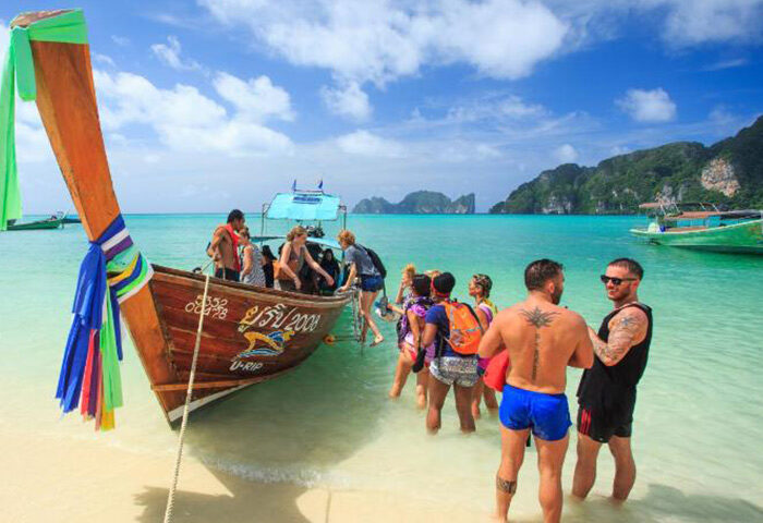 Koh Phi Phi's Cobble Beach Hotel: Beachfront scene with gay travelers disembarking a longtail boat on a sunny day. Tropical paradise.