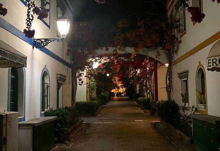 Street view near Paso Chico Gay Hotel, Gran Canaria. Budget gay hotel near Yumbo Center with bougainvillea and street light at night.
