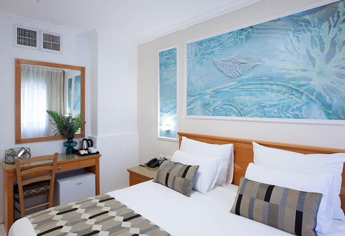 Armon Hayarkon Hotel room in Tel Aviv near Hilton Beach. Budget gay hotel room with bed, desk, and sea-themed artwork. Best gay travel choice.