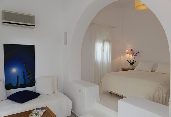 Elena Hotel, Mykonos Town. Budget gay hotels offer. All-white room with bed, couch, and archway. Ideal for gay travelers. Updated space.