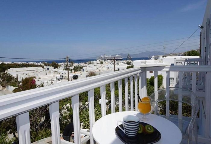 Elena Hotel, Mykonos Town. Private balcony view of sea. Budget gay hotel with breakfast, coffee, and juice. White buildings, blue sky.