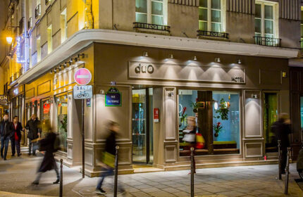 Duo Hotel, a cheap gay hotel in Paris city center. Exterior view at night. Pedestrians walk by the Rue du Temple hotel entrance.