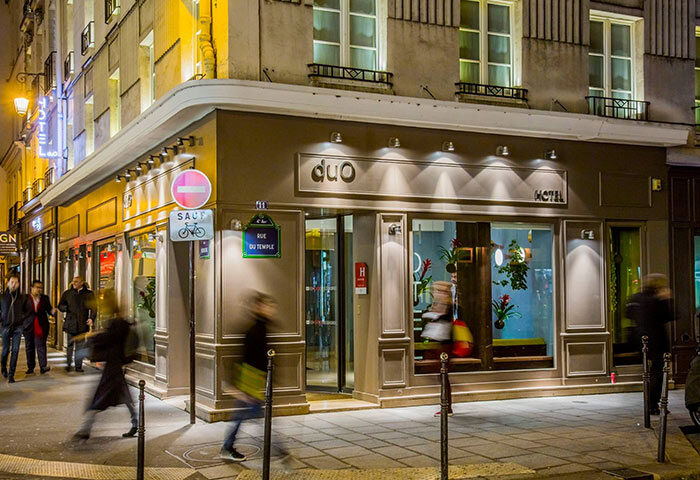 Duo Hotel, a cheap gay hotel in Paris city center. Exterior view at night. Pedestrians walk by the Rue du Temple hotel entrance.
