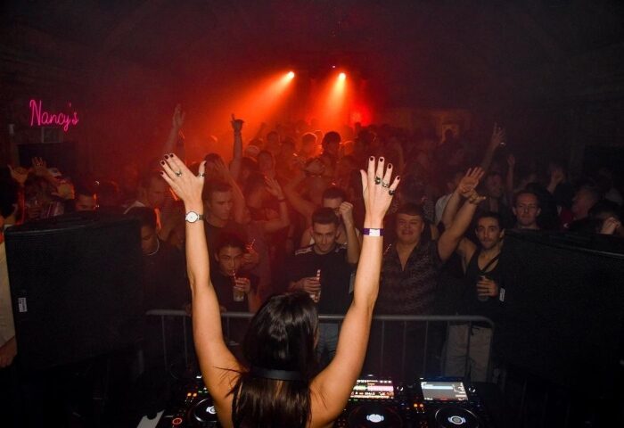 Feel It @ Omeara: DJ with raised hands at a London gay night. Party crowd visible in the background. Best Friday gay bar scene.