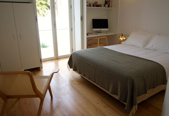 Bedroom at The Late Birds Lisbon Gay Urban Resort, a men-only hotel. Features a bed, chair, desk with computer, and minimalist decor.