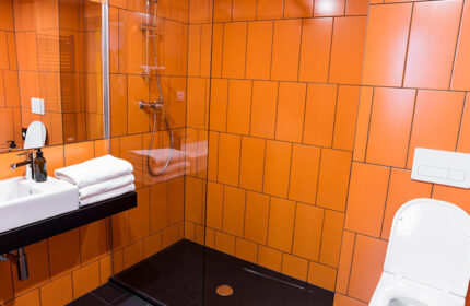 Bathroom of gay-friendly hostel in Prague. Orange tiles, black shower, white sink, toilet. Best gay travel advice. Meetme23.
