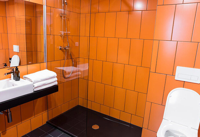 Bathroom of gay-friendly hostel in Prague. Orange tiles, black shower, white sink, toilet. Best gay travel advice. Meetme23.